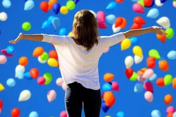 femme aux bras tendus au milieu de ballons colorés en signe de bonheur